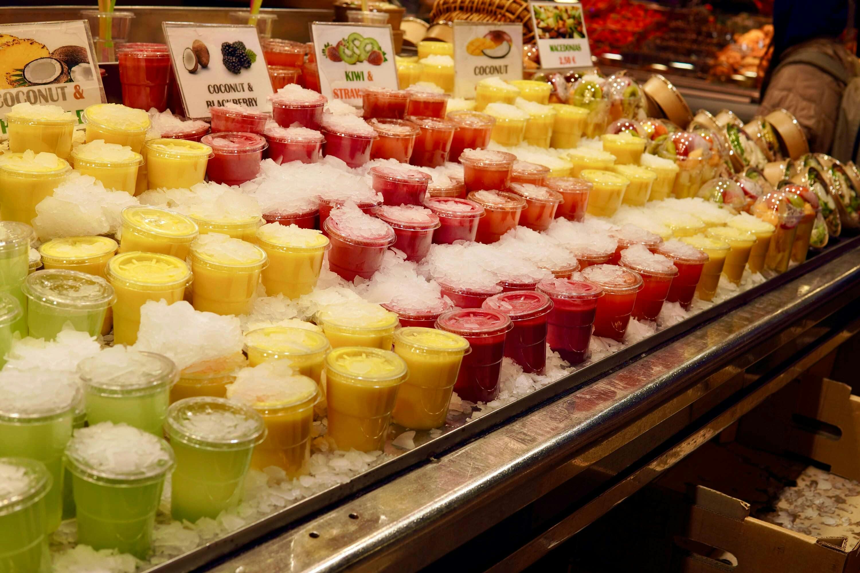 Rows of colorful cups on juice sitting in an ice cooler at a market